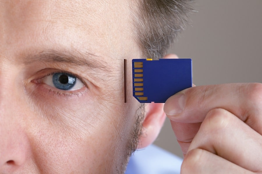 A person feels good while holding a blue SD card next to their forehead, symbolizing the capture of lasting memories. The image focuses on the face and the hand holding the card, with the eye in sharp detail against a neutral-toned background.