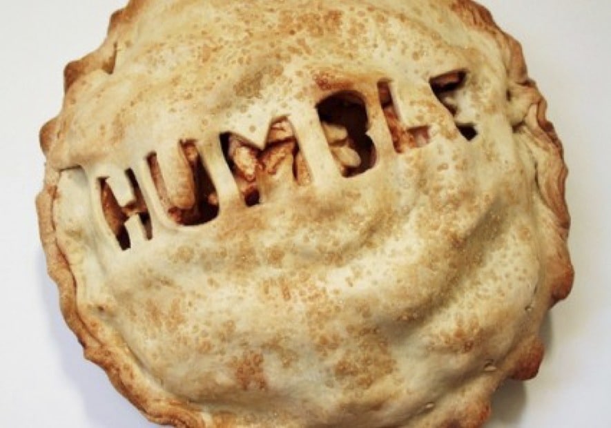 A baked pie with a golden crust has the word "HUMBLE" cut out in capital letters on top, exposing the filling beneath—a perfect slice of acceptance served fresh.