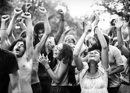 In a black and white photo, a diverse group of people is captured outdoors, joyfully raising their arms and cheering. The scene evokes feelings of unity and camaraderie, reminiscent of the joyful vibe in "I Get By With a Little Help." Trees standing tall in the background add to the celebratory atmosphere.