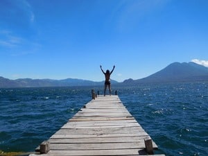 Standing triumphantly at the end of a wooden pier over the serene Lake Atitlan, with arms raised against a clear blue sky, one feels an invigorating sense of accomplishment. Majestic mountains embrace the scene, making it perfect for a transformative neurosculpting retreat.