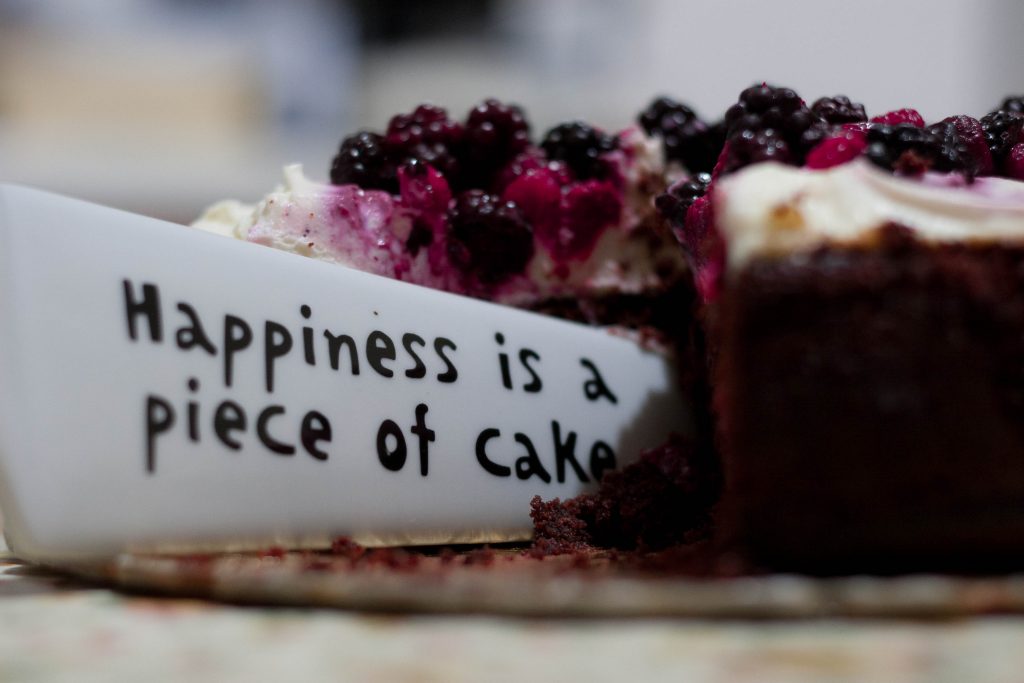 A chocolate cake topped with mixed berries is on a plate. A slice is cut out and placed on a triangular server inscribed with "Lisa's Note of the Day: Happiness is a piece of cake." The focus is on the elegant server and delectable cake.