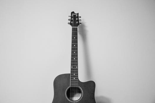 Black and white image of an acoustic guitar, reminiscent of Lisa's Note of the Day, leaning against a plain wall. The partially visible guitar's neck extends upward like thought patterns, with six tuning pegs contrasting against the white background.