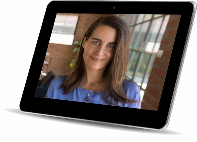 A woman with long brown hair smiles confidently at the camera, exuding personal power. She's wearing a blue top, and indoors with a large window and brick wall in the background. The image is displayed on a tablet screen, capturing her inspiring mindset.