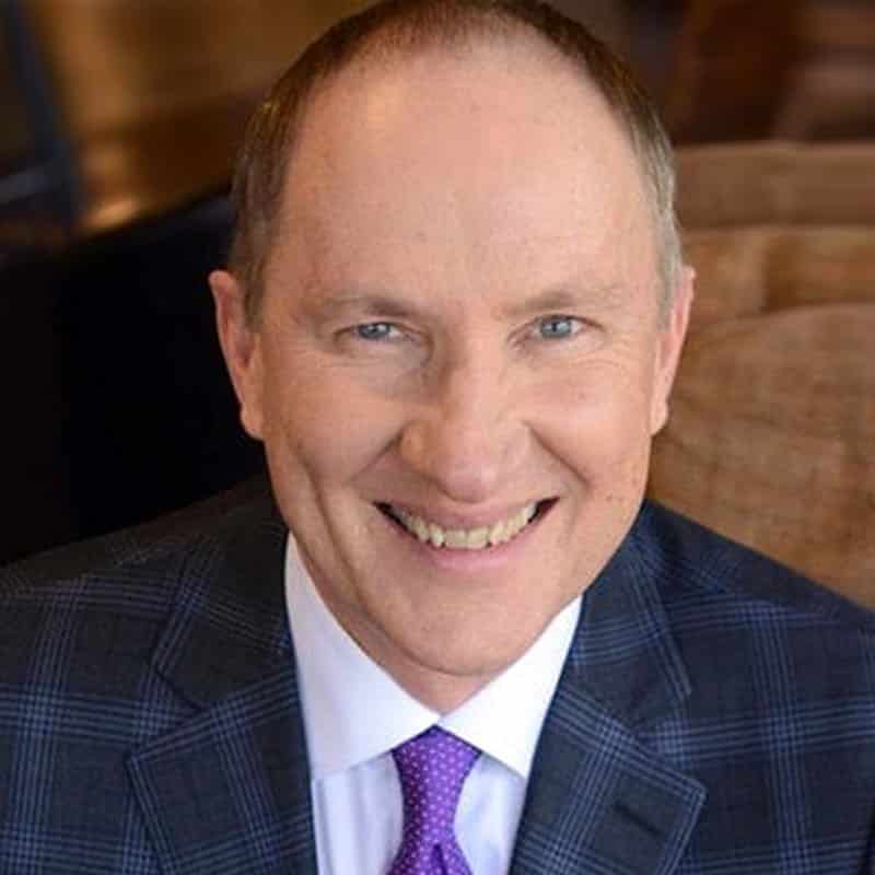 Seated indoors, a smiling person exudes personal power in a checkered suit jacket and purple tie, embodying the mindset of success.