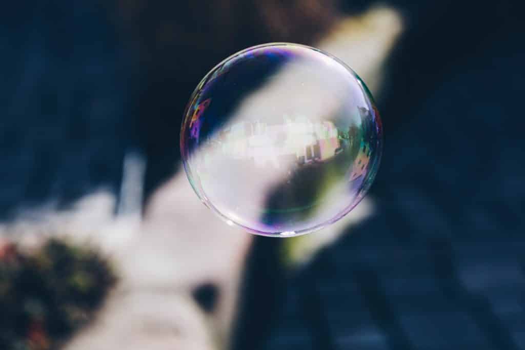 Close-up of a single, translucent soap bubble gracefully floating against a blurred background. The bubble, much like finding your center, reflects surrounding colors and light, creating a subtle spectrum of hues on its surface.