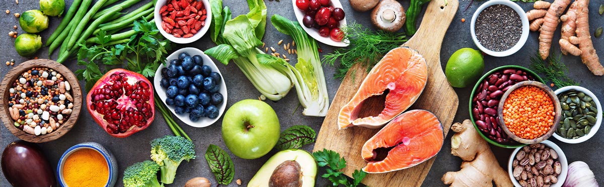 A vibrant assortment of foods perfect for healthy brain nutrition: salmon fillets on a wooden board, surrounded by fruits, vegetables, nuts, seeds, and spices like blueberries and pomegranate. Inspired by Erin Livers and ICNT for a nourishing gray surface display.