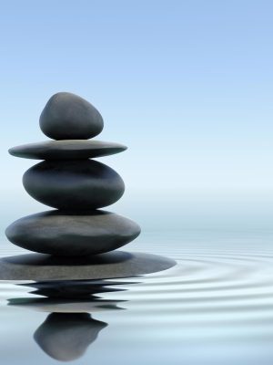 A stack of smooth stones balances on a tranquil water surface, creating gentle ripples and inviting a sense of stress release. The sky is clear and blue, reflecting a calming atmosphere.