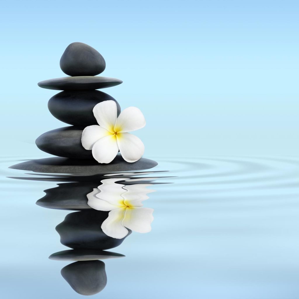 Smooth black stones stacked on a calm water surface, with a white plumeria flower resting atop, evoke tranquility. The blue sky reflects in the water, creating gentle ripples that seem to release stress, washing it away with each soothing wave.