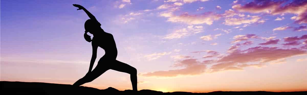 Silhouette of a person performing a yoga pose, with one arm extended upward, against a vibrant sunset sky with colorful clouds—a perfect scene for an introductory class in the art of relaxation and balance.